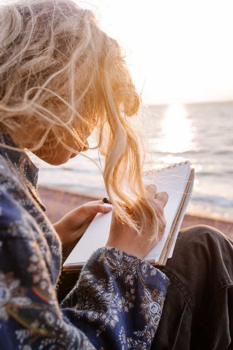 A woman journaling by the sea at golden hour