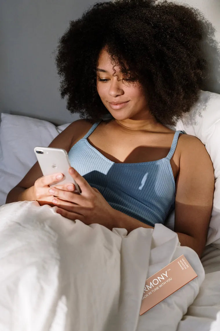 A woman relaxing in bed, checking her Hormony results on her phone